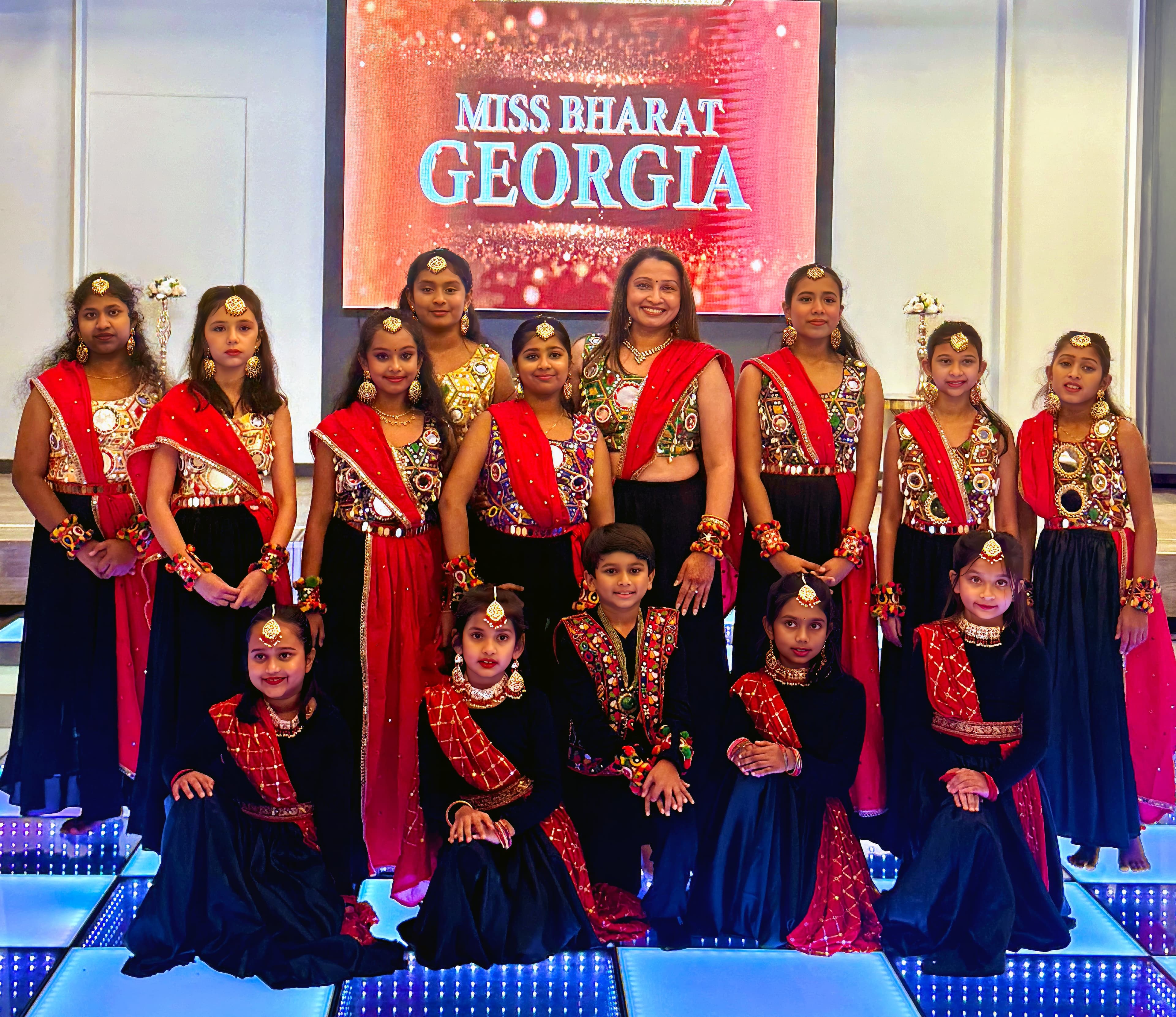 Garima Dance Academy students with the instructor in red and black Bollywood costumes on a Miss Bharat Georgia stage