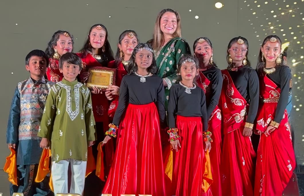 Lil’ Stars students with the instructor in red and black traditional dance outfits, holding a recognition plaque